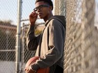 Homme avec lunettes connectées Ray-Ban Meta, sweat à capuche, tenant un ballon de basket. Style sportif et polyvalent.