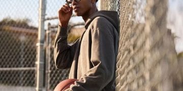 Homme avec lunettes connectées Ray-Ban Meta, sweat à capuche, tenant un ballon de basket. Style sportif et polyvalent.