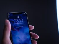 Main tenant un iPhone affichant l'écran de verrouillage avec l'heure 23:10 et une image abstraite. Évoque l'Apple Intelligence en France.