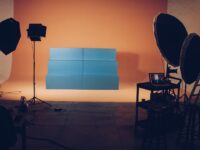 Studio vidéo professionnel avec fond orange, structure bleue, éclairages studio et ordinateur portable affichant un montage.