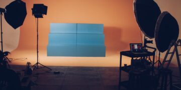 Studio vidéo professionnel avec fond orange, structure bleue, éclairages studio et ordinateur portable affichant un montage.