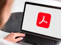 Person using a laptop displaying the Adobe Acrobat logo. AI gives Acrobat a brain for your PDFs.