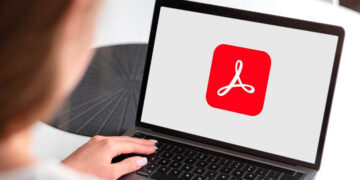 Person using a laptop displaying the Adobe Acrobat logo. AI gives Acrobat a brain for your PDFs.