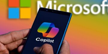 Main tenant un smartphone affichant le logo Copilot IA sur fond sombre. Le logo et le nom Microsoft sont en arrière-plan coloré et flou.