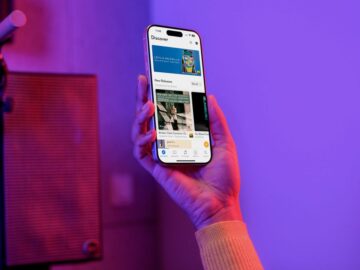 Main tenant un smartphone affichant l'app Qobuz, section Discover, avec albums. Micro et enceinte en arrière-plan. Contexte IA musicale.