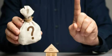 Main tenant un sac d'argent avec un point d'interrogation, une maison en bois et un doigt pointé. Symbolise l'accès au crédit bancaire via Machine Learning et IA.