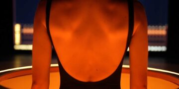Dos d'une personne scannée par un appareil futuriste orange lumineux, symbolisant le Midjourney Scanner et l'IA pour la santé.
