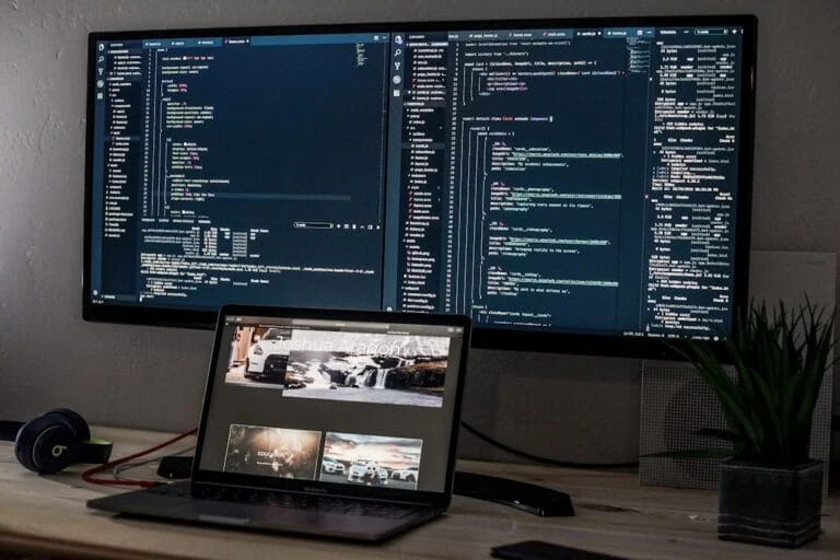 Écran d'ordinateur affichant du code de développement web et un laptop avec un site. Représente l'IA et la programmation.
