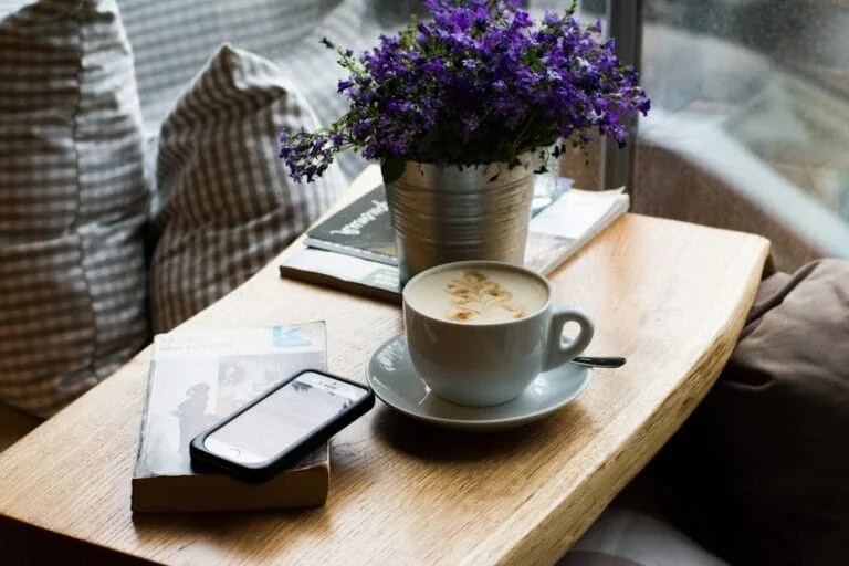 Scène cosy: cappuccino, smartphone sur un livre et fleurs violettes sur une table en bois. L'IA s'intègre au quotidien.