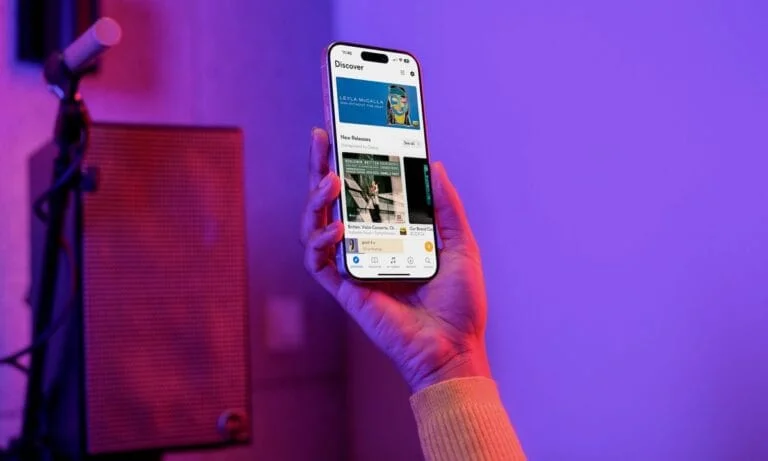 Hand holding a Qobuz smartphone displaying "Discover" and "New Releases", on a purple background with microphone and speaker. Music AI context, q.jpeg.