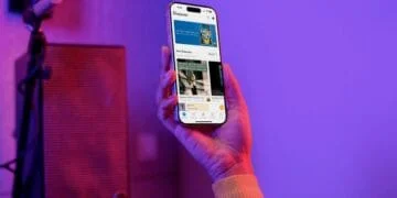 Main tenant un smartphone affichant l'app Qobuz "Discover" pour la musique. Micro et enceinte en arrière-plan, lumière violette et rouge.